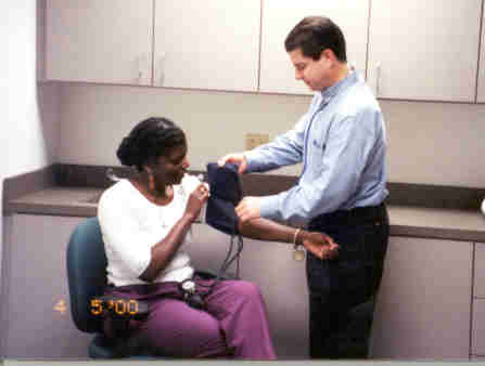 picture of a young man helper assisting the woman with placement of the blood pressure cuff onto her upper arm